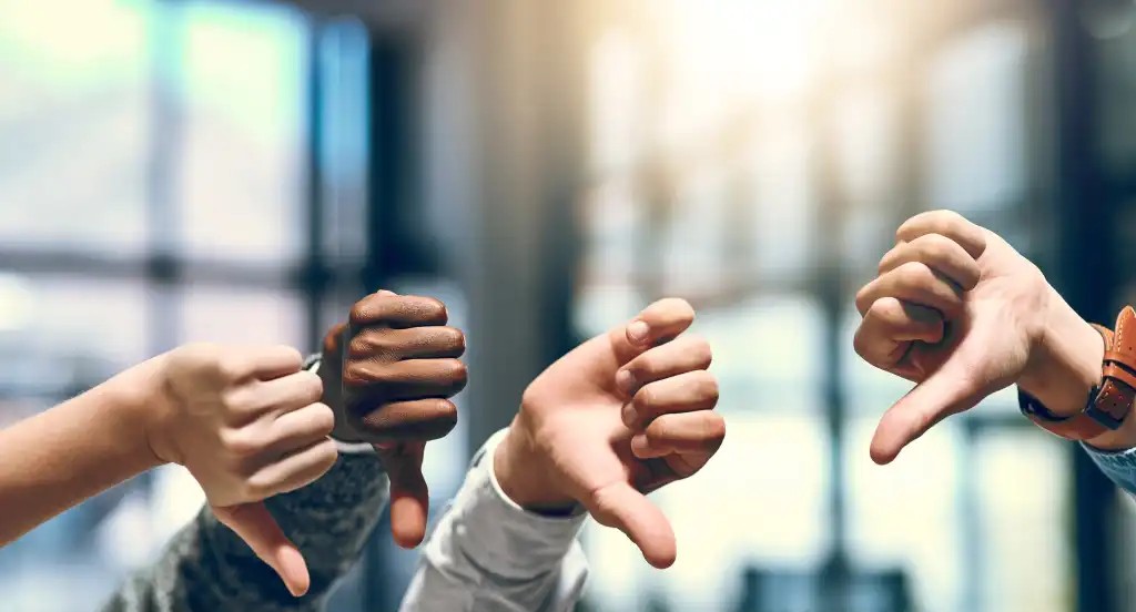 four hands raised with thumbs down in front of window with blurred light